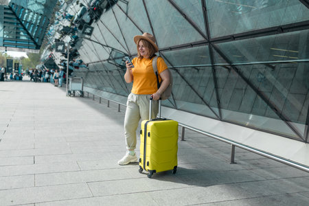 Happy traveling Caucasian 30s woman in stylish casual clothes and hat uses mobile smartphone, checking trip destination on Internet. Female waiting at flight gates for plane boarding, smiling have a vacation trip. High qualityの写真素材