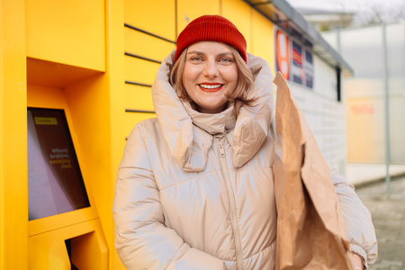 Woman receiving parcel from automatic post box using smartphone outdoors. Modern delivery technologies concept. High quality photoの写真素材