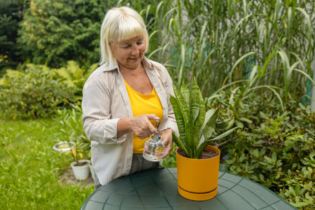 Smiling elderly woman gardener is watering flower plant outdoors.Pretty female taking care of garden. Watering flowers from watering can in summer time. Free time hobbies for seniors.の写真素材