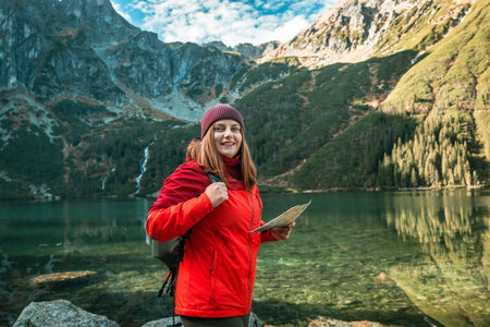 Shot of lost woman traveler with map and backpack relaxing outdoor with rocky on Morskie Oko lake. Woman traveler explorer with backpack hiking to the top of the mountain. Hiking travel and adventure in Poland, Tatryの写真素材