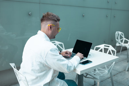 Happy traveling Caucasian man in stylish clothes uses mobile smartphone and laptop, checking trip destination on Internet. Male waiting at flight gates for plane boarding, smiling have a vacation trip. High qualityの写真素材