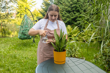 Young woman with watering can and green houseplant in garden in summer timeの写真素材