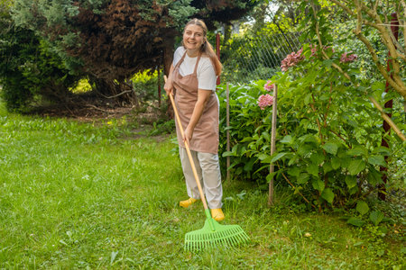 Raking leaves. Picture of happy woman working with tools in the garden, preparing the garden for winter, spring. Taking care of the garden. High quality photoの写真素材