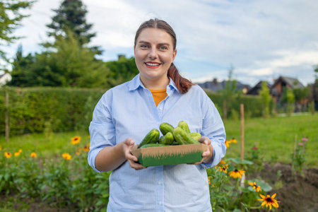 Young woman, farmer, worker holding in hands homegrown harvest of fresh orange cucumber. Private garden, orchard, natural economy, hobby and leisure concept. High quality photoの写真素材