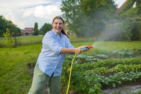 30s woman watering fresh plants growing at home vegetable garden. Gardener taking care of plants at the backyard of her house. Concept of sustainability and growing organic. High quality photoの写真素材