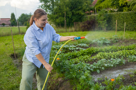 30s woman watering fresh plants growing at home vegetable garden. Gardener taking care of plants at the backyard of her house. Concept of sustainability and growing organic. High quality photoの写真素材