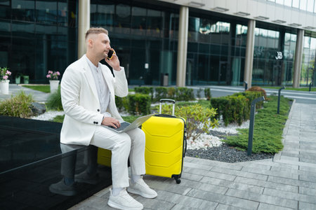 Portrait of a handsome young businessman traveling with bag and talking on phone outdoors near a business centre. High quality photoの写真素材