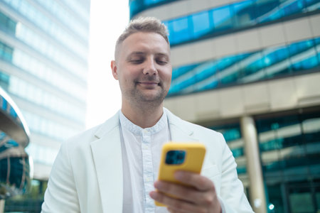 Focused young corporate worker investor businessman walking and using mobile phone outdoors near a business centre. High qualityの写真素材