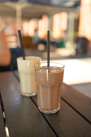 Two pink fruit milk cocktails in glasses with black tubes spiral pattern for milkshakes, cocktails, juices stand on table in street cafe. Bokeh background, backdrop, High quality photoの写真素材