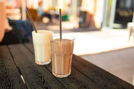 Two pink fruit milk cocktails in glasses with black tubes spiral pattern for milkshakes, cocktails, juices stand on table in street cafe. Bokeh background, backdrop, High quality photoの写真素材