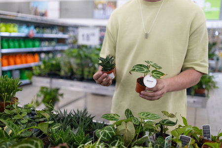 Portrait of smiling young bearded man in green t shirt holding while choosing plants in home goods store. Plant, nature, shopping concept. High quality photoの写真素材