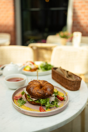 Fresh croissant sandwiches with vegetables, meat and cheese on a table with seeds and flour. Cup of aromatic tea in the background. High qualityの写真素材