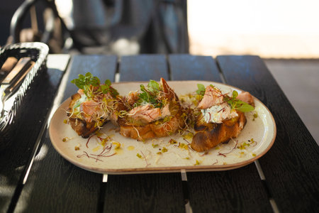 Fresh avocado toast with smoked salmon and poached eggs with grilled vegetables on plate on wooden table in city cafe. Healthy food and lifestyle. High qualityの写真素材