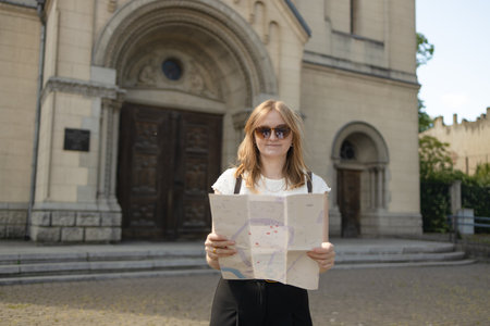 Young blonde Caucasian female tourist smiling confidently with backpack, traveling, looking at city map on street. Plan your route from your location to your destination. Traveling in Europe. High qualityの写真素材