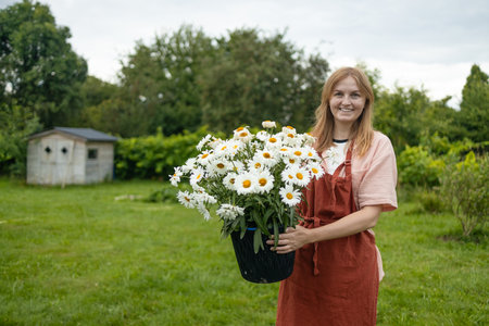Caucasian woman holding a freshly collected bunch of white daisies in a beautiful spring backyard. Gathering wildflowers and enjoying a nature. High quality photoの写真素材