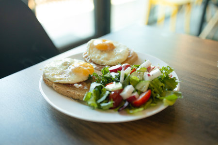 Two toast with poached egg and salad with spinach, cherry tomatoes and mozzarella, ingredients on a white plate on breakfast table, appetizing vegetarian dish, white background, close up . High quality photoの写真素材