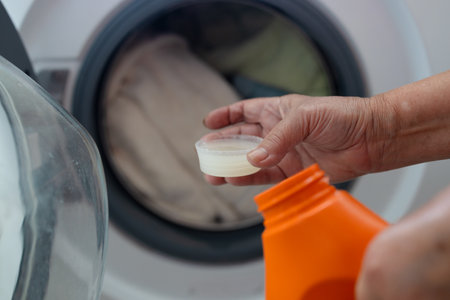 Woman pouring fabric softener from bottle into cap near washing machine in bathroom. High quality photoの写真素材