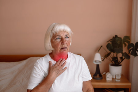 Heart attack. Sick senior adult elderly woman touching the neck feeling unwell coughing with sore...