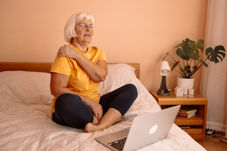 Mature woman have a shoulder pain at home office. Elderly woman shoulder pain osteochondrosis.の写真素材