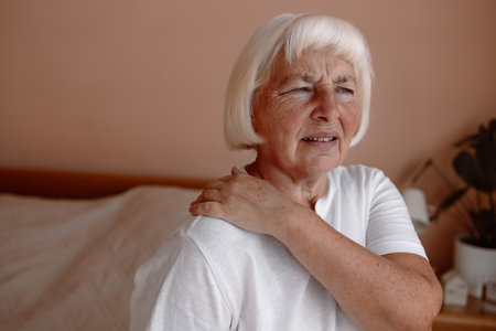 Mature woman have a shoulder pain at home office. Elderly woman shoulder pain osteochondrosis.の写真素材