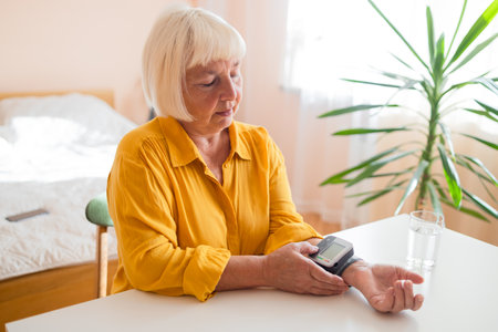 Senior woman with hypertension measuring blood pressure herself at home. Sad Mature lady measure blood pressure using tonometer. Everyday health check-up. High quality photoの写真素材