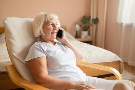 Portrait of attractive successful elderly woman using mobile talking on a cellphone while relaxing at home.の写真素材