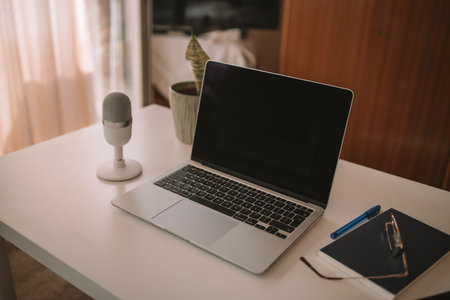 Closeup of a professional podcast microphone resting on a desk in a recording ready podcasting home studio. Selective focus of podcast equipment in empty room, ready to be used for online streaming. High quality photoの写真素材