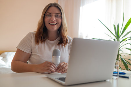 Young woman student relax sit on sofa with cat holding laptop looking at computer screen online learning on pc. Female sit at home talk on video call with friend or relative, happy millennial biracial female speak online usingの写真素材