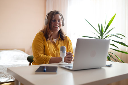 Young woman student relax sit on sofa with cat holding laptop looking at computer screen online learning on pc. Female sit at home talk on video call with friend or relative, happy millennial biracial female speak online usingの写真素材