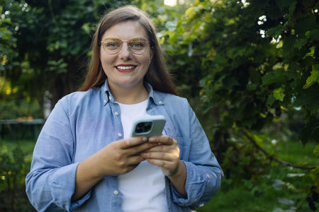 Caucasian woman smiling confident using smartphone at backyard. Young woman browsing Internet on a...
