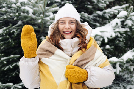 Positive Caucasian european woman takes selfie on her phone in frosty winter forest. Video call via mobile Internet while traveling on sunny day in natureの写真素材
