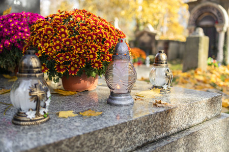 Tombstones decorated with colorful seasonal chrysanthemum flowers in cemetery during religious christian traditional autumnal event at a cemetery in Poland during All Saints Day, Zaduszki day, and Day of the Dead. Lit candles illuminate the graves at a Christian cemetery at night.の写真素材