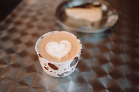 Chocolate cup of cappuccino and cake on a table in the cafe terrace outside. Atmospheric coffee time. Heart shaped dessert decorations. High quality photoの写真素材