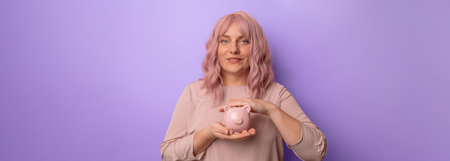 Young caucasian woman smiling holding a piggybank for investment on light lilac backgroundの写真素材