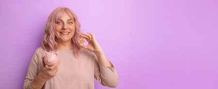 Young caucasian woman smiling holding a piggybank and bitcoin for investment on light lilac backgroundの写真素材