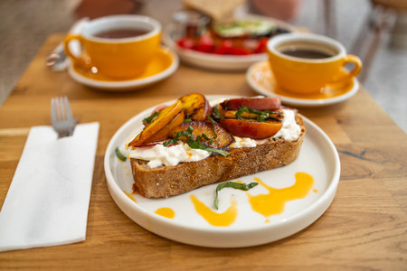 Toast with cream cheese, fresh juicy peach, almond and honey on a wooden tray. Healthy summer appetizer or snack. High quality photoの写真素材