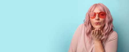Beautiful woman with makeup and long pink hair blows kiss, demonstrates her good feelings isolated over blue background. Young pretty female model makes air kiss. High quality photoの写真素材