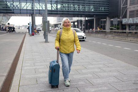 Senior female tourist in airport hold suitcase valise passport ticket schedule to check flight departure gate. Travel and tourism concept, people with backpack on shoulders. High quality photoの写真素材