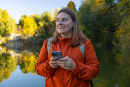 Traveler hiker 30s woman holding smartphone in a hand and using GPS app with trekking in autumn mountains outdoor.の写真素材