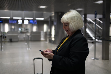 Travel Caucasian senior 60s 50s woman traveler text messaging on cell phone at the airport, waiting for departure at the airport on vacation holiday.の写真素材