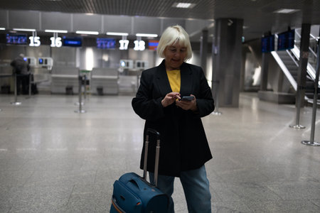Travel Caucasian senior 60s 50s woman traveler text messaging on cell phone at the airport, waiting for departure at the airport on vacation holiday.の写真素材