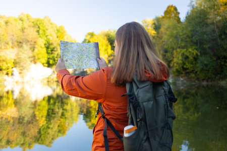 Wanderings. Stylish young woman traveler with a backpack, holds a map, explores hiking trails in the mountains. The concept of travel, vacation.の写真素材