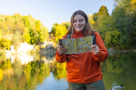 Wanderings. Stylish young woman traveler with a backpack, holds a map, explores hiking trails in the mountains. The concept of travel, vacation.の写真素材