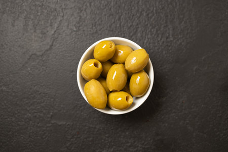 Whole green olives in a bowl on black background. Top view, close-up. High quality photoの写真素材