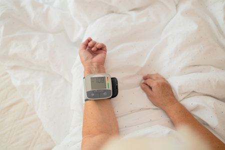 Close-up of wrist blood pressure monitor on female hand measuring pulse and blood pressure in a bed. Health care and check up concept.の写真素材