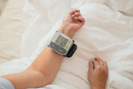 Close-up of wrist blood pressure monitor on female hand measuring pulse and blood pressure in a bed. Health care and check up concept.の写真素材
