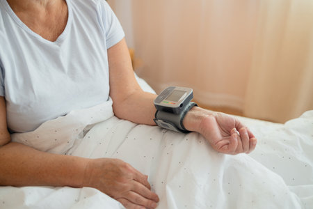 Close-up of wrist blood pressure monitor on female hand measuring pulse and blood pressure in a bed. Health care and check up concept.の写真素材