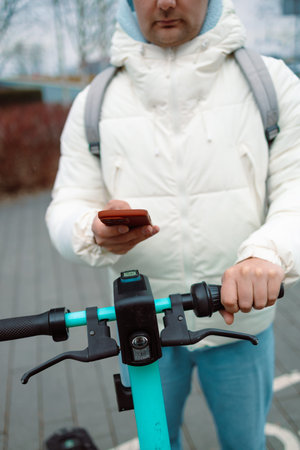 Handsome man using smartphone app. Guy approaches an electric scooter and using mobile phone app NFC...