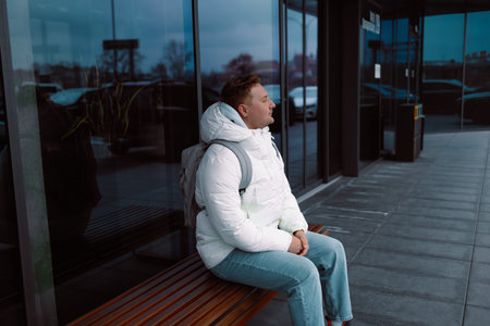 Full length of sad upset pensive thoughtful guy backpacker sit on modern bench outside in city...