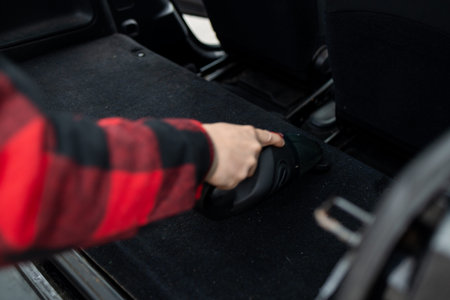 Details of car vacuum cleaning. Professional cropped male worker using wet vacuum cleaner for dirty car interior. Auto car service cleaning the drivers seat, cleaning and vacuuming concept. High quality photoの写真素材